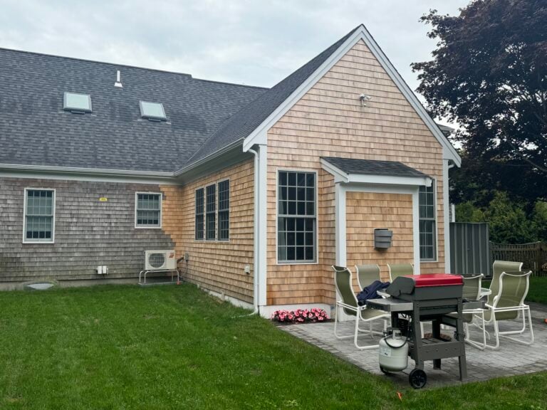 A cedar-shingled Cape Cod home with a summer patio and outdoor living space, built by Custom Crafted Homes
