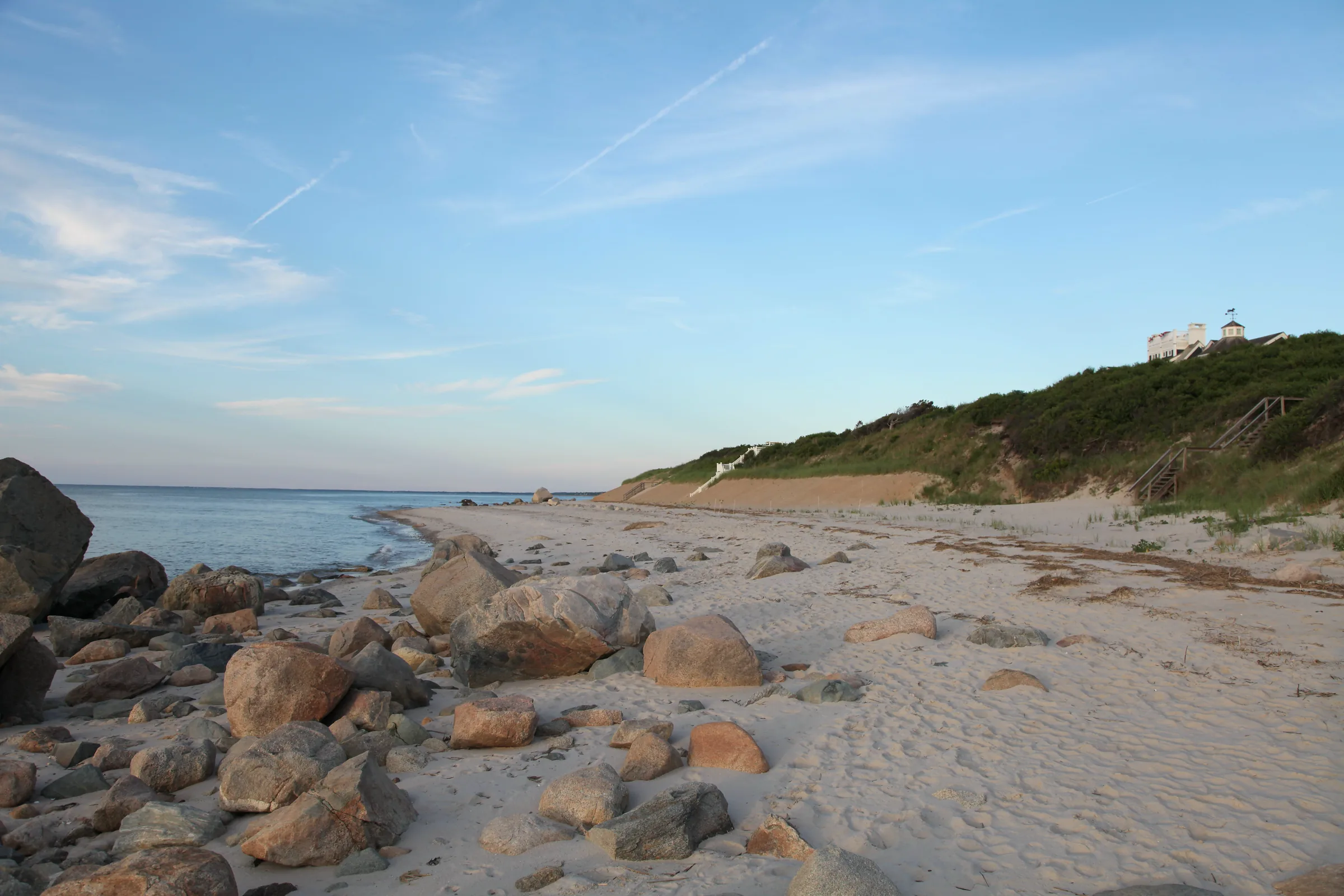 Golden-hour light over a Dennis, Massachusetts bayside beach, a shingled Cape home on the bluff above the shore.