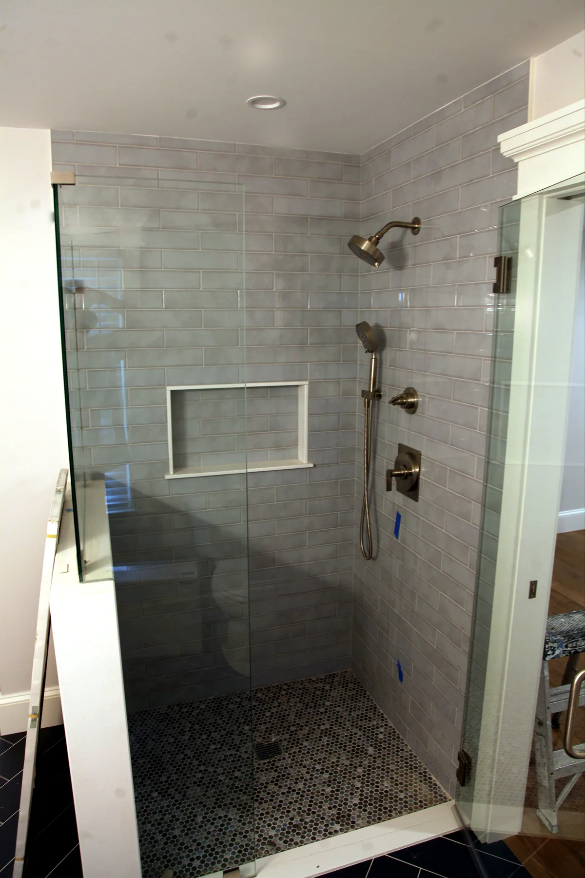 Custom tiled shower with glass enclosure, niche, handheld shower, and pebble tile floor