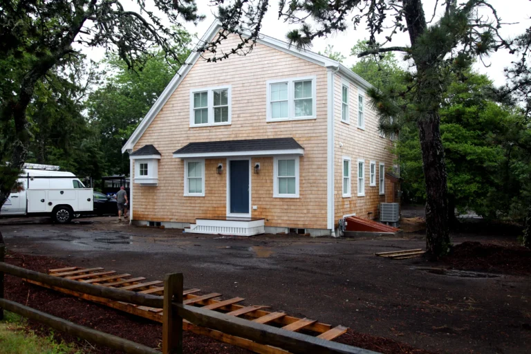New cedar-shingle Cape Cod home exterior with blue front door and white trim after rain