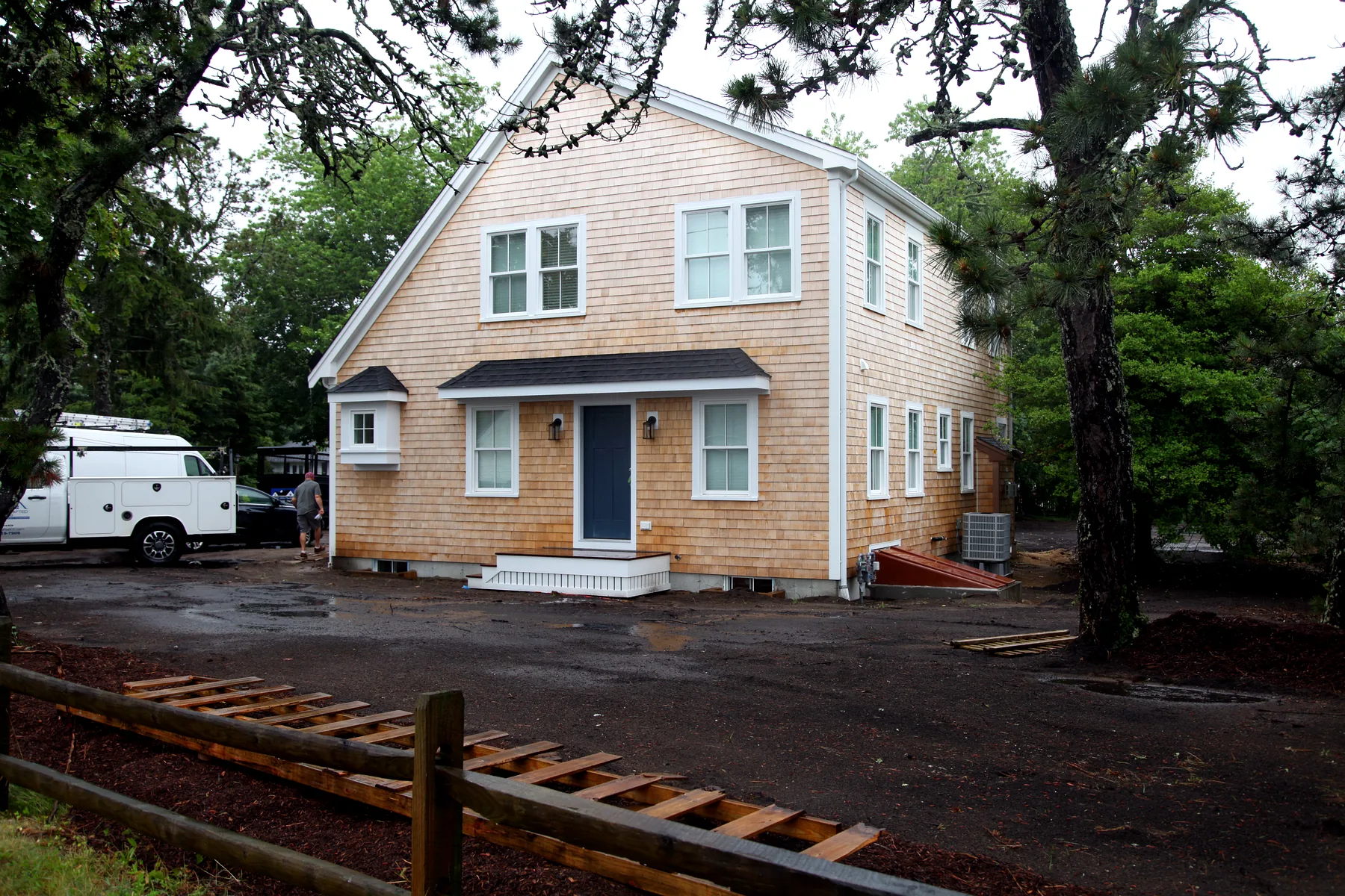 New cedar-shingle Cape Cod home exterior with blue front door and white trim after rain