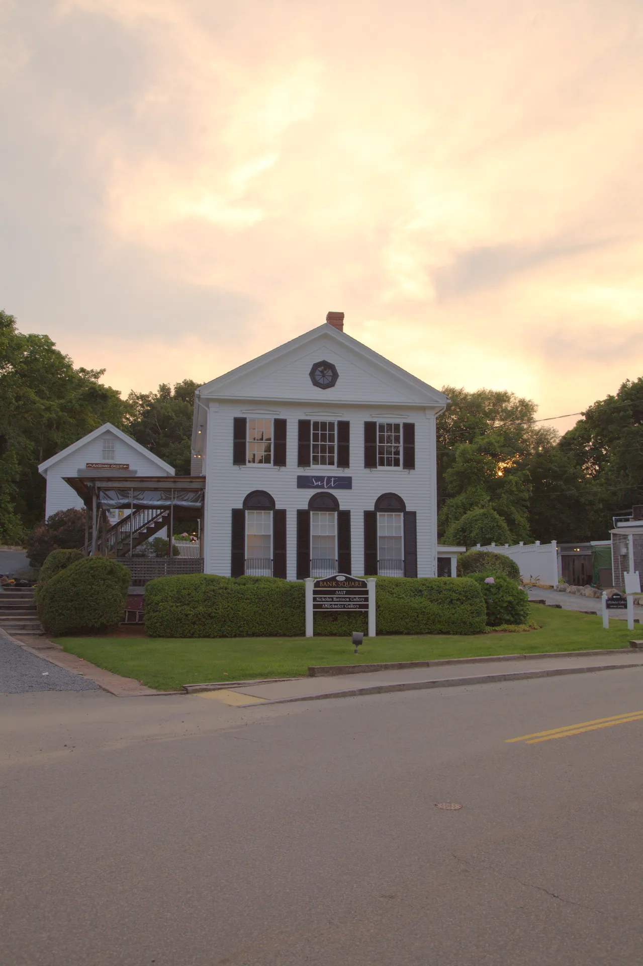 A white clapboard Greek Revival building with black shutters and an octagonal gable window in Wellfleet Center, under a peach sunrise sky.