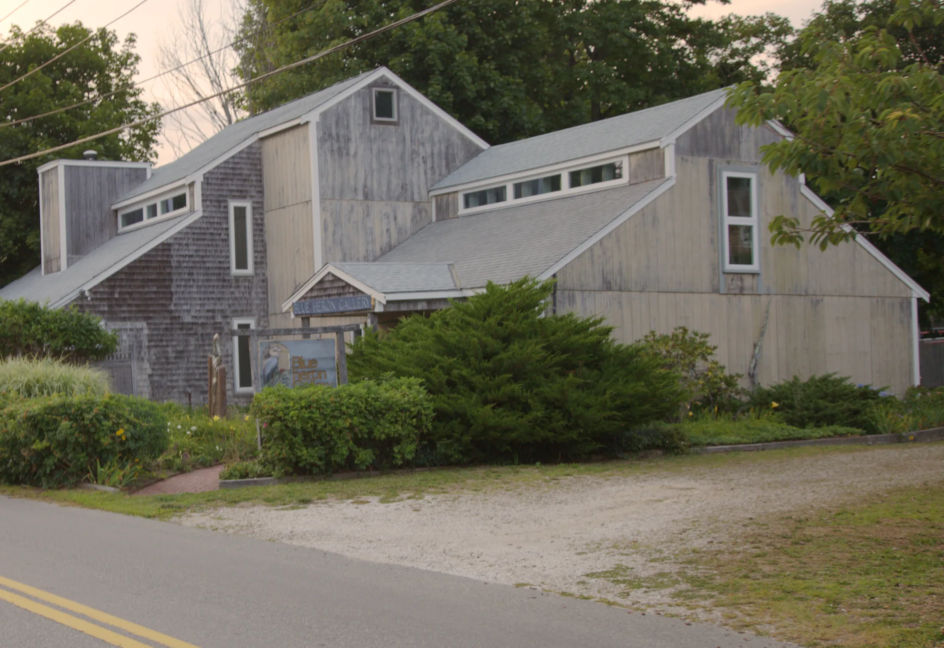 A weathered cedar-shingle and vertical-board building in Wellfleet Center at sunrise, with shed dormers, clerestory windows and steep gable ends.